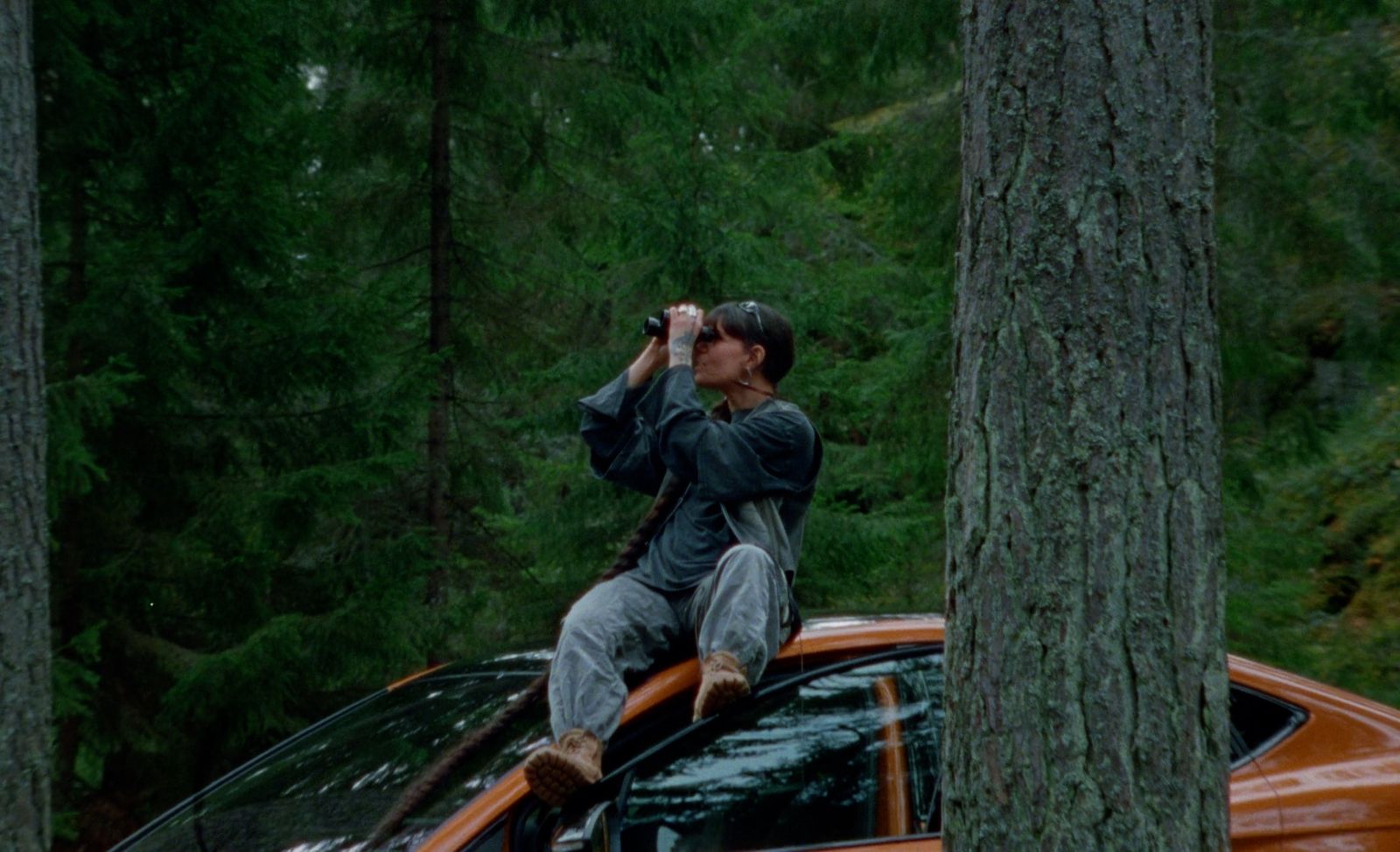 a man sitting on top of a car in the woods