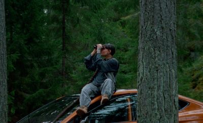 a man sitting on top of a car in the woods