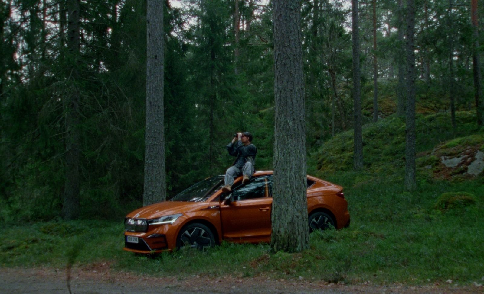 a man standing on top of an orange car in the woods