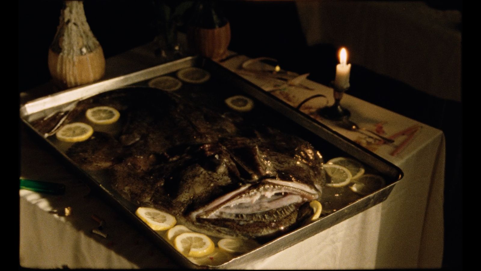 a fish on a table with lemons and a candle