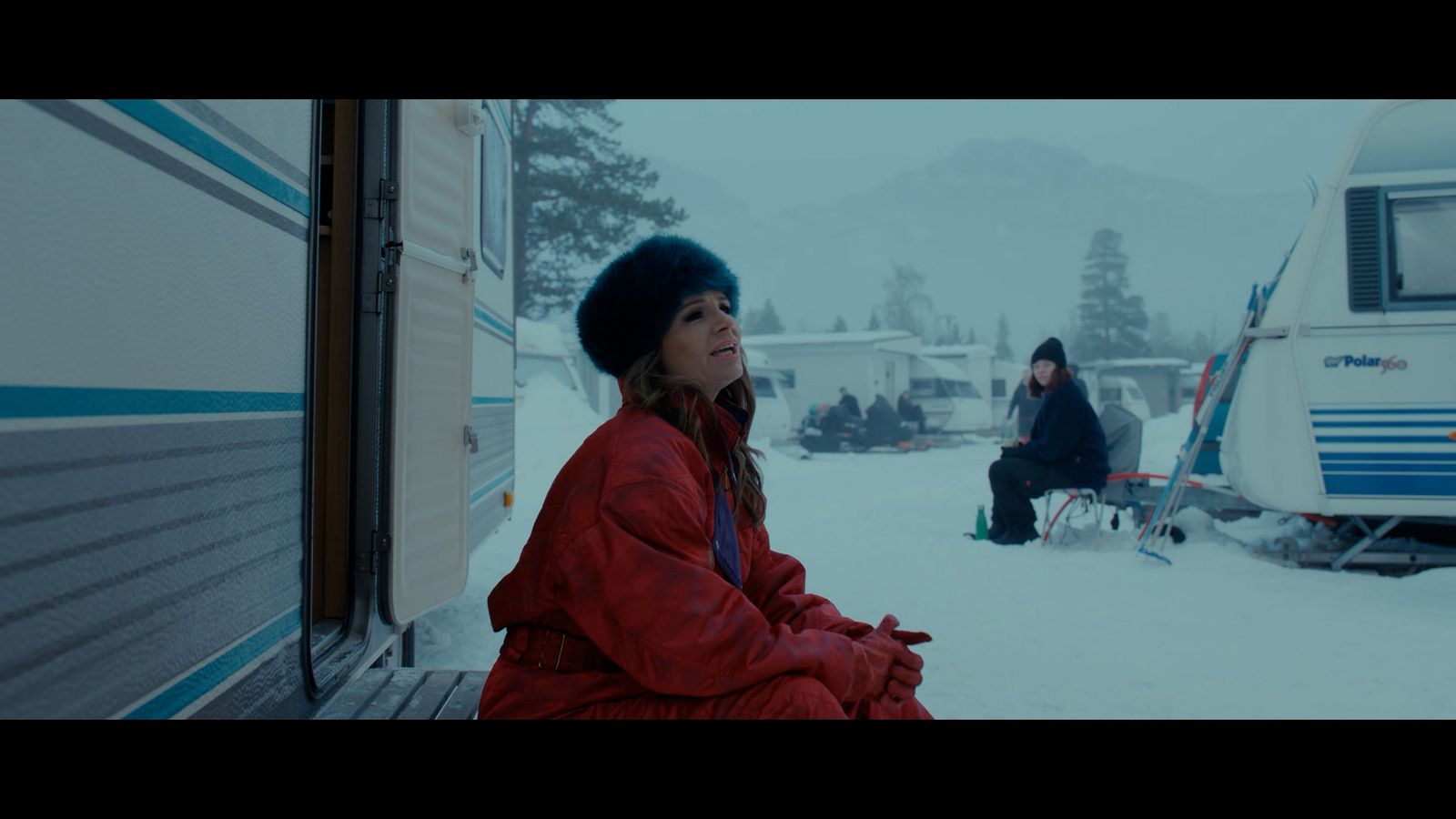 a woman sitting outside of a trailer in the snow