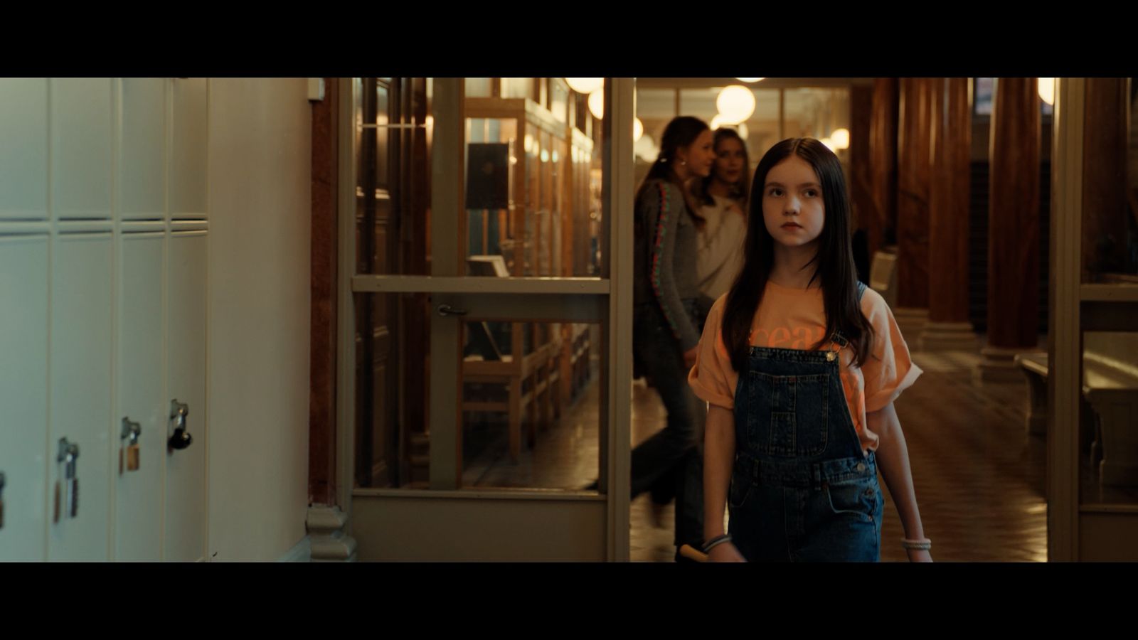 a girl in overalls standing in a hallway