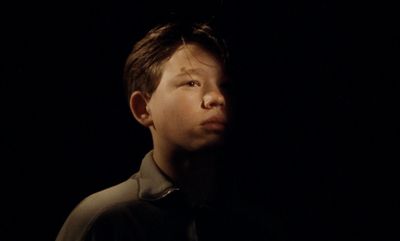 a young boy standing in the dark with his eyes closed