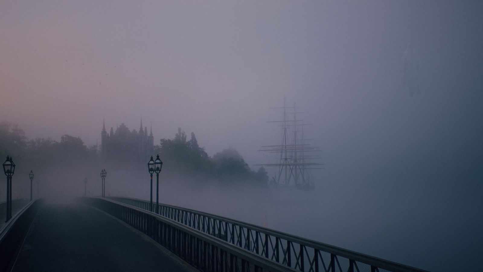 a foggy bridge with a tall ship in the distance