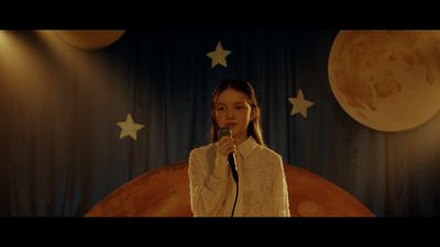 a girl singing into a microphone in front of a curtain