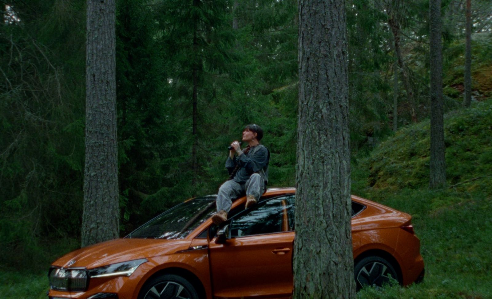 a man sitting on top of an orange car in the woods