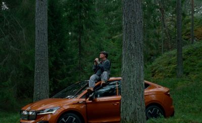 a man sitting on top of an orange car in the woods