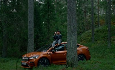 a man sitting on top of an orange car in the woods