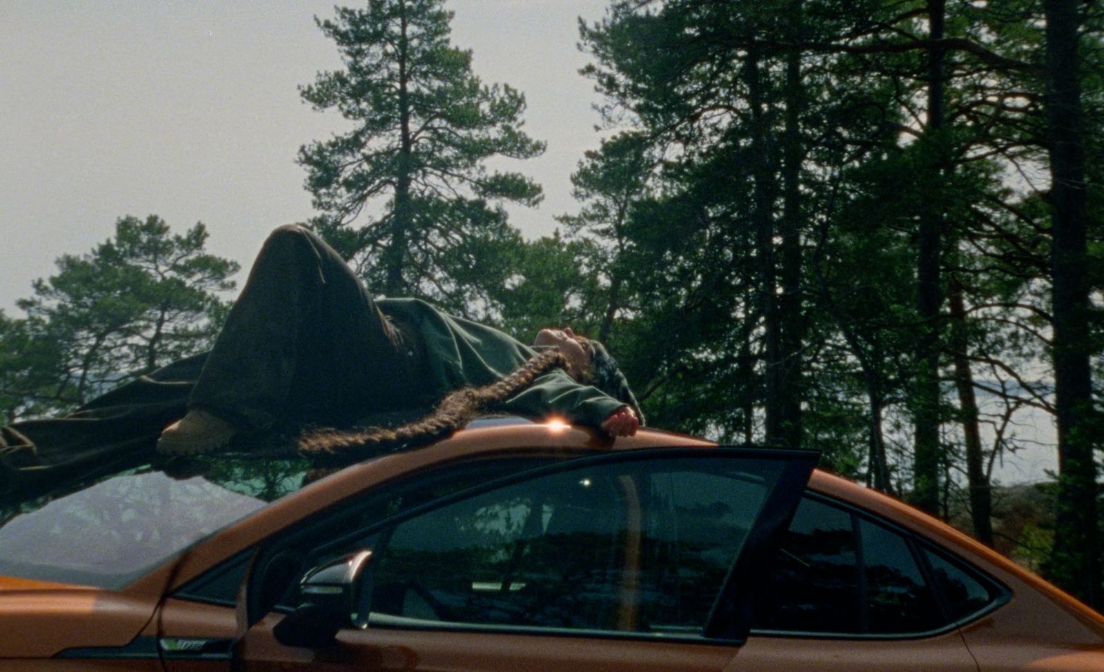 a person laying on top of a car in the woods