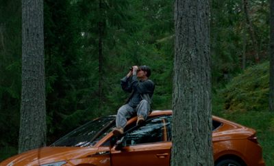 a man sitting on top of a car in the woods