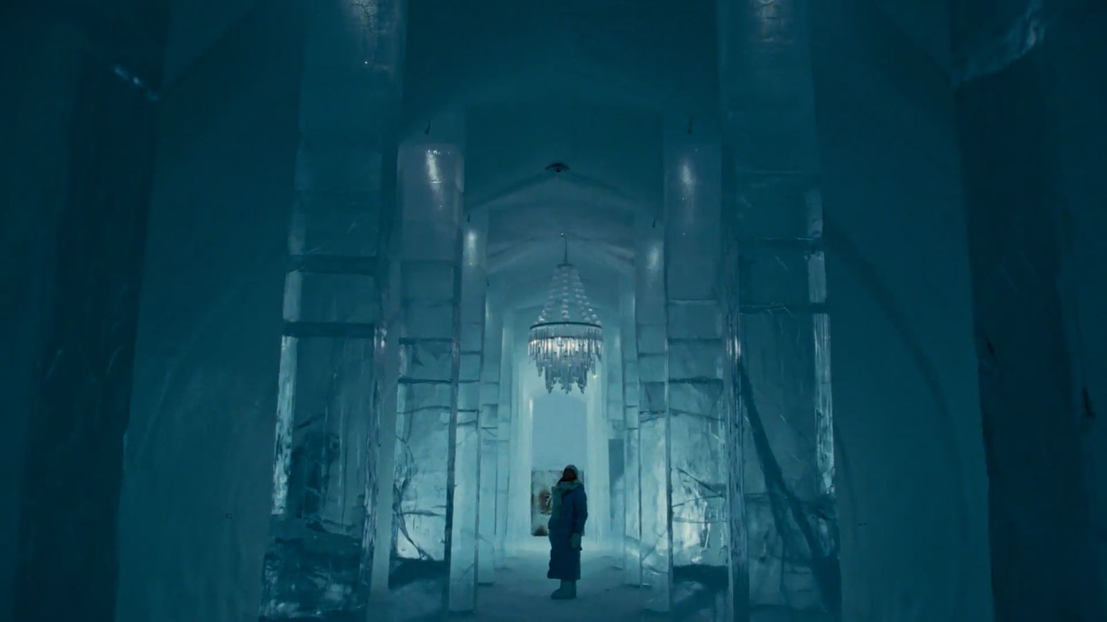 a person standing in an ice tunnel with a chandelier hanging from the ceiling