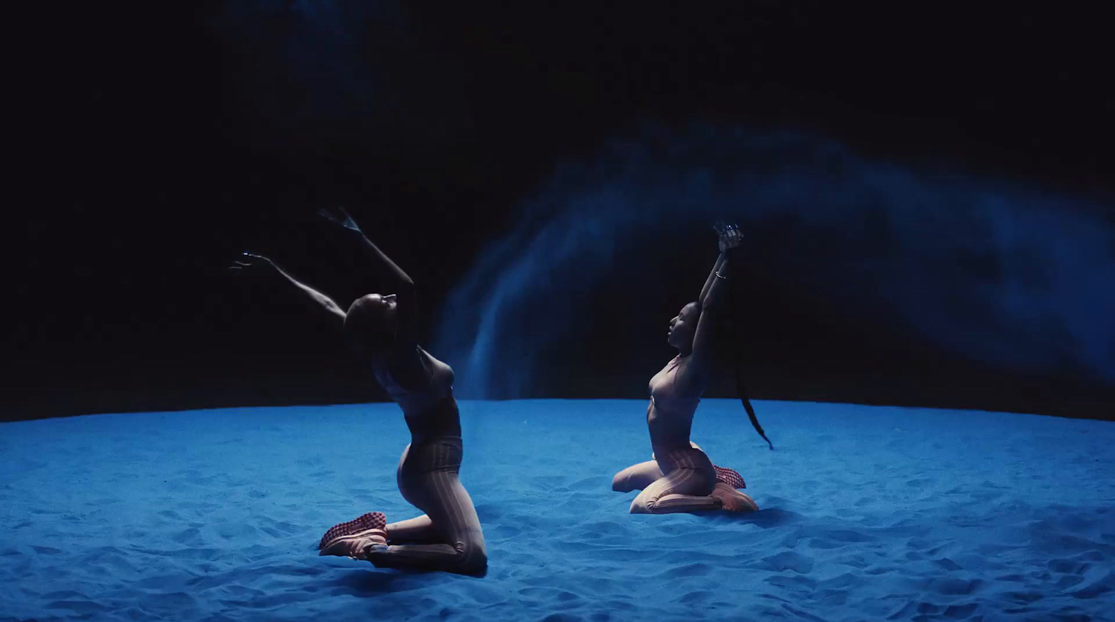 two naked women sitting in the sand with their hands in the air