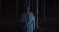 a man in a blue coat standing in a dark forest