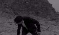 a man in a suit and tie standing on a rocky hill