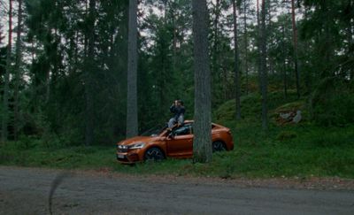 a man standing on top of an orange car in the woods