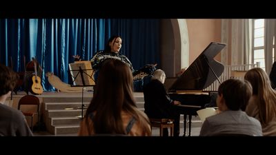 a woman standing at a piano in front of a group of people