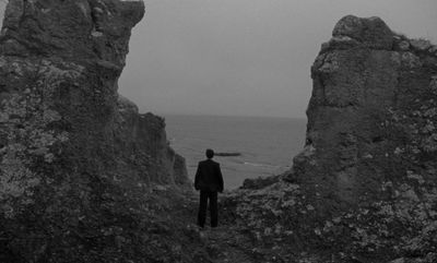 a man standing on top of a rocky cliff near the ocean