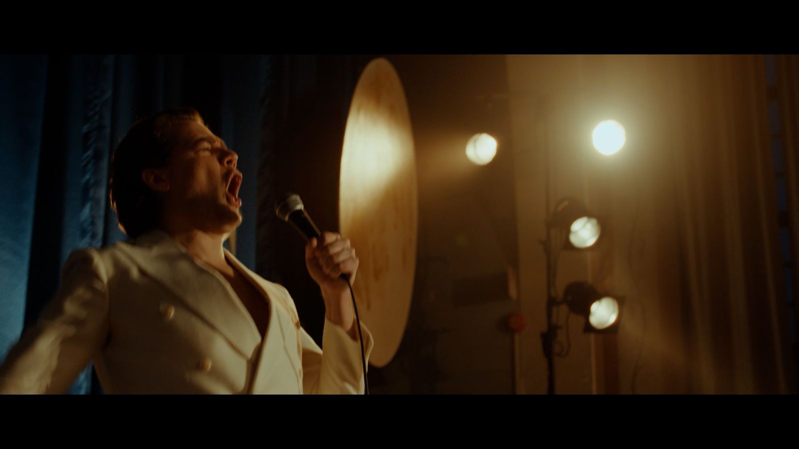 a man in a white suit singing into a microphone