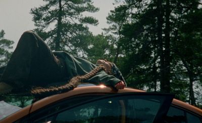 a man laying on top of a car in the woods