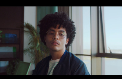 a young man with glasses sitting in front of a window