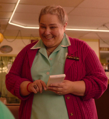 a woman in a red cardigan smiles as she holds a cell phone