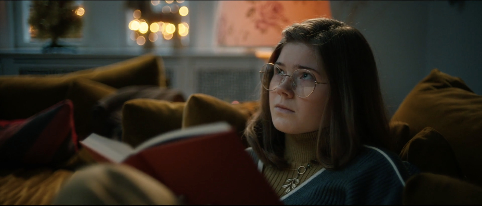 a girl with glasses reading a book on a couch