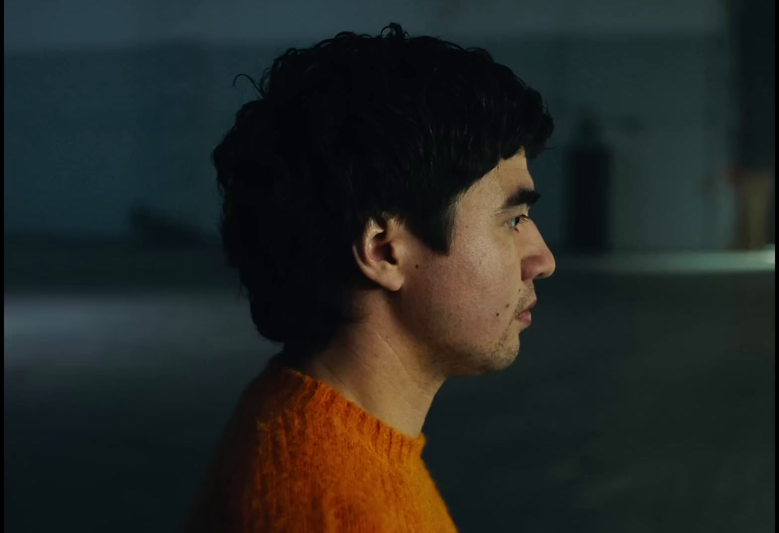 a man in an orange sweater looking off into the distance