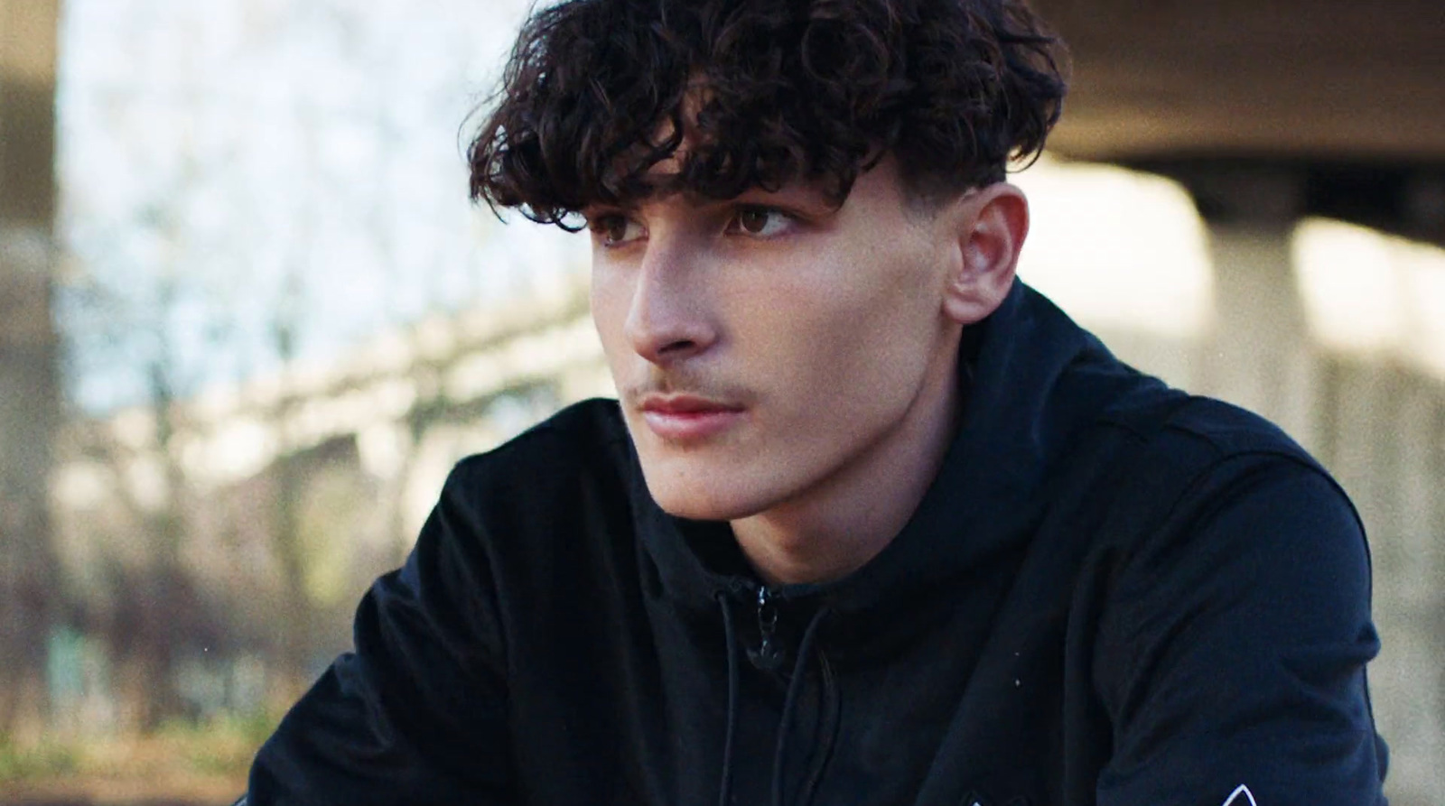 a young man with curly hair wearing a black hoodie