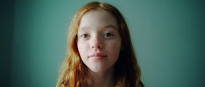 a young girl with red hair is looking at the camera