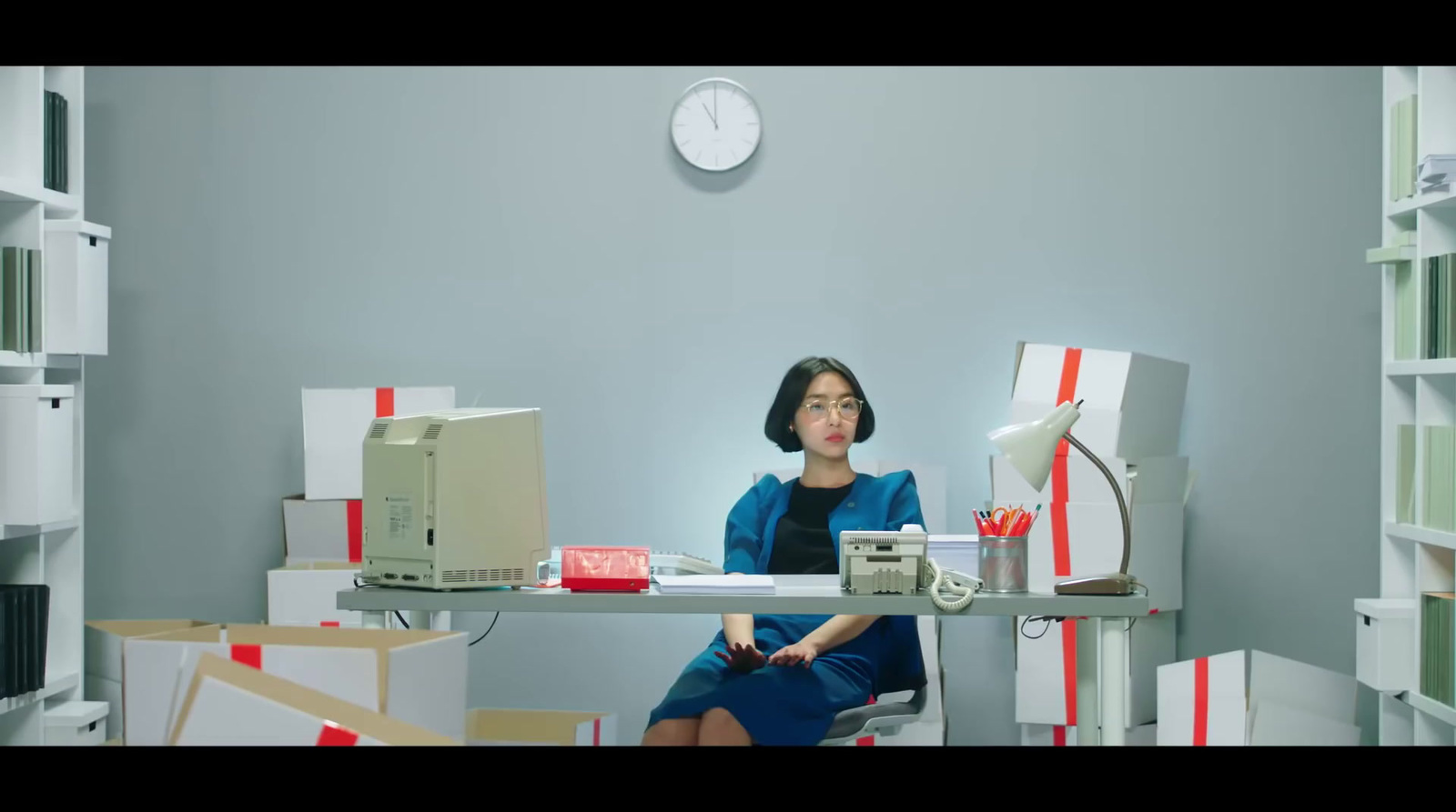 a woman sitting at a desk in a room filled with boxes