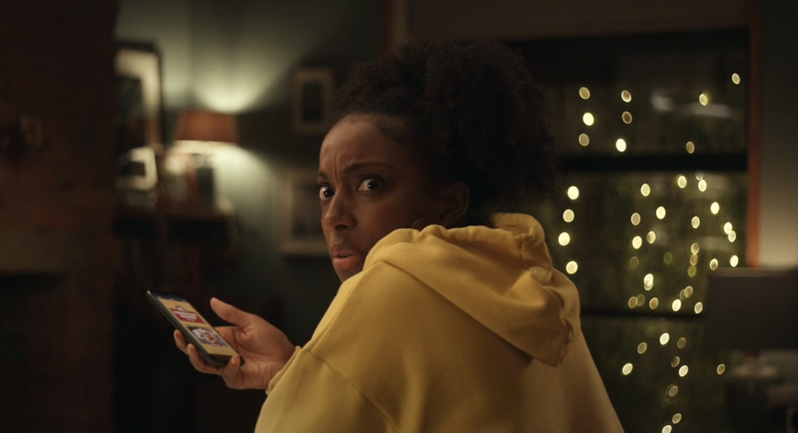 a woman in a yellow hoodie holding a cell phone