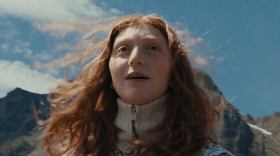 a woman with red hair standing in front of a mountain