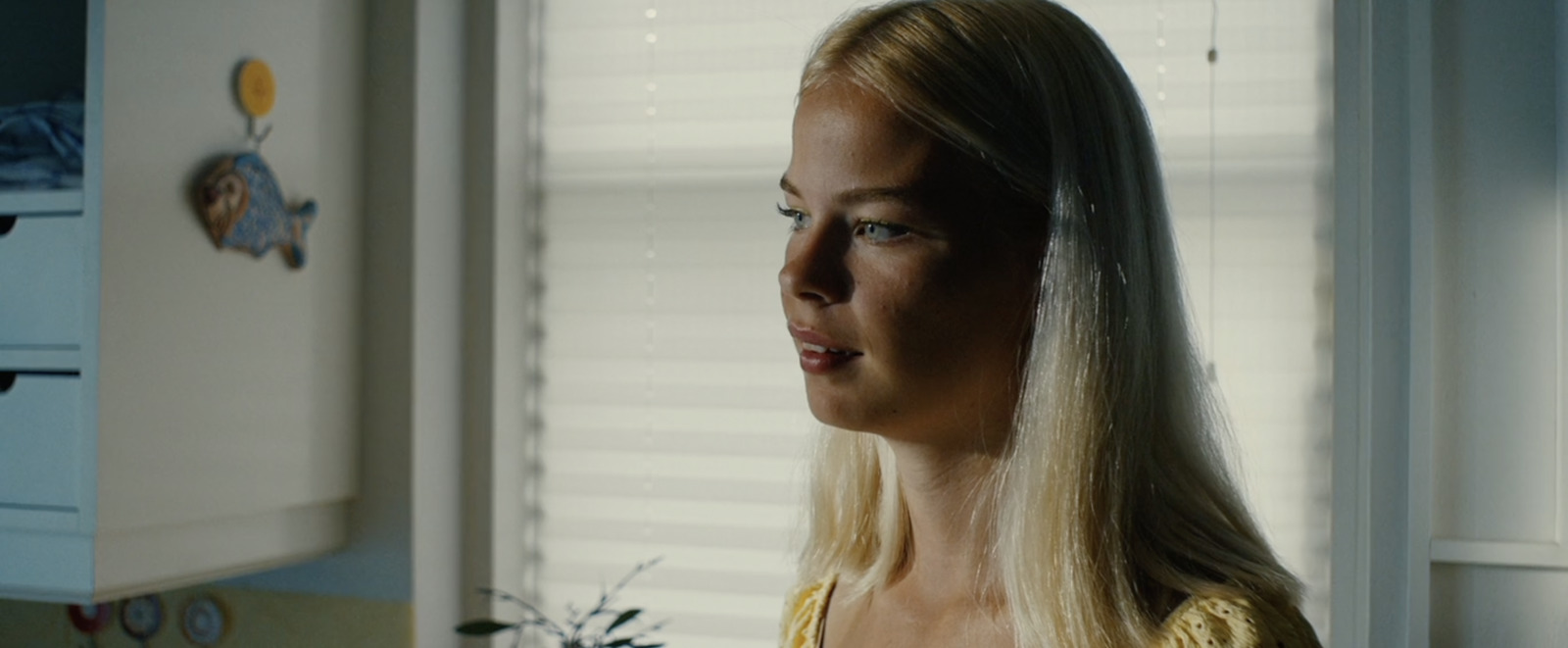 a blonde woman in a yellow top standing in a kitchen