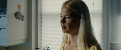 a blonde woman in a yellow top standing in a kitchen