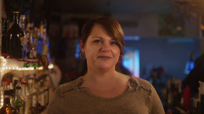 a woman standing in front of a bar filled with liquor bottles