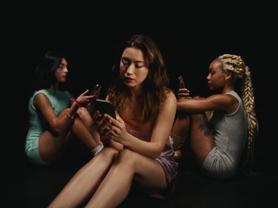 three women sitting on the ground looking at a cell phone