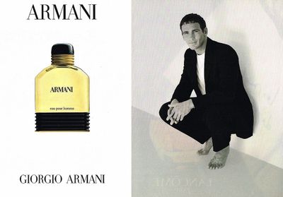 a man in a black suit sitting next to a bottle of perfume