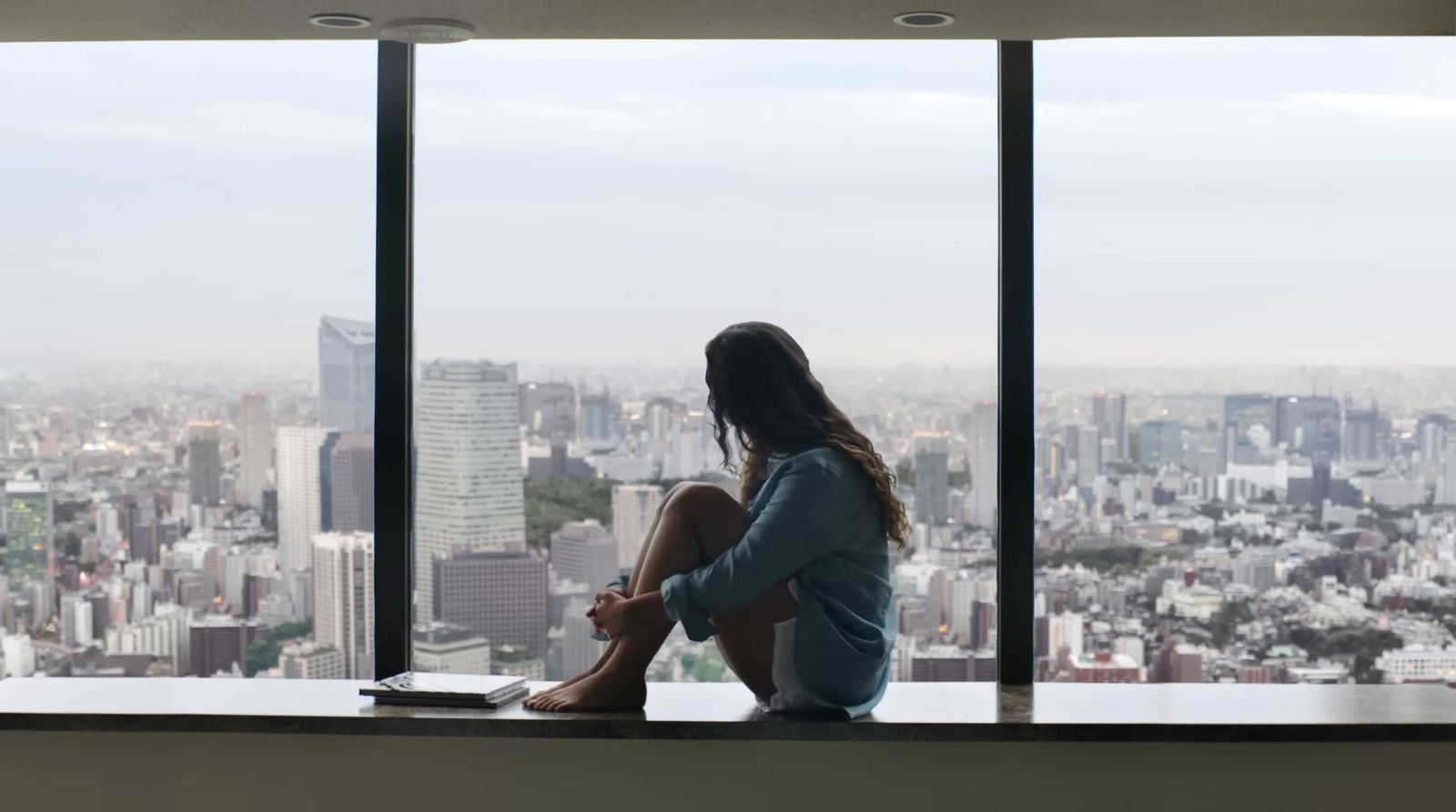 a woman sitting on a window sill looking out at a city