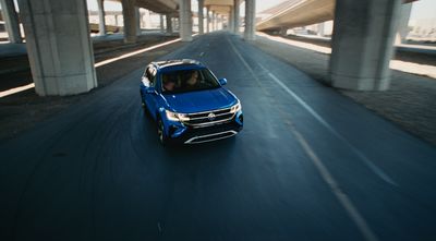 a blue car driving down a highway under a bridge