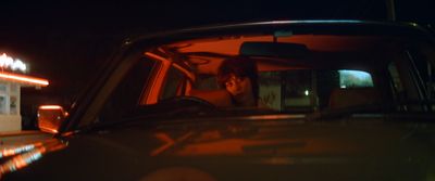 a man sitting in a car at night talking on a cell phone