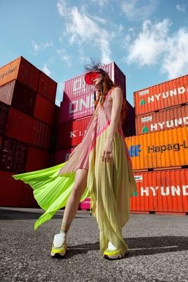 a woman in a yellow dress standing in front of a stack of shipping containers
