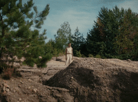 a man walking down a dirt road next to a forest