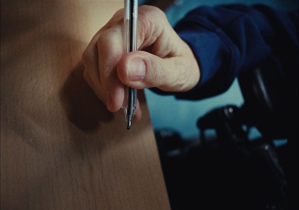 a person holding a pen and writing on a piece of wood