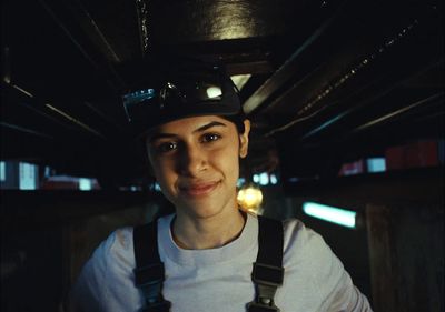 a woman wearing a hat and suspenders in a dark room