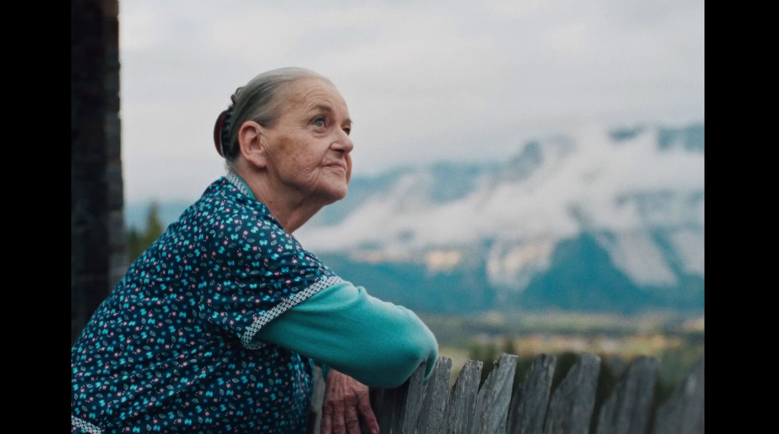 a woman leaning on a wooden fence with mountains in the background