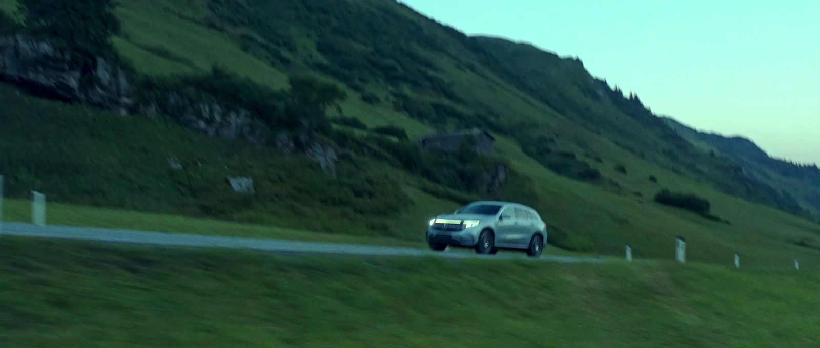 a car driving down a road next to a lush green hillside