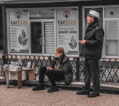 two people sitting on a bench in front of a store
