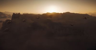 a group of birds flying over a mountain at sunset