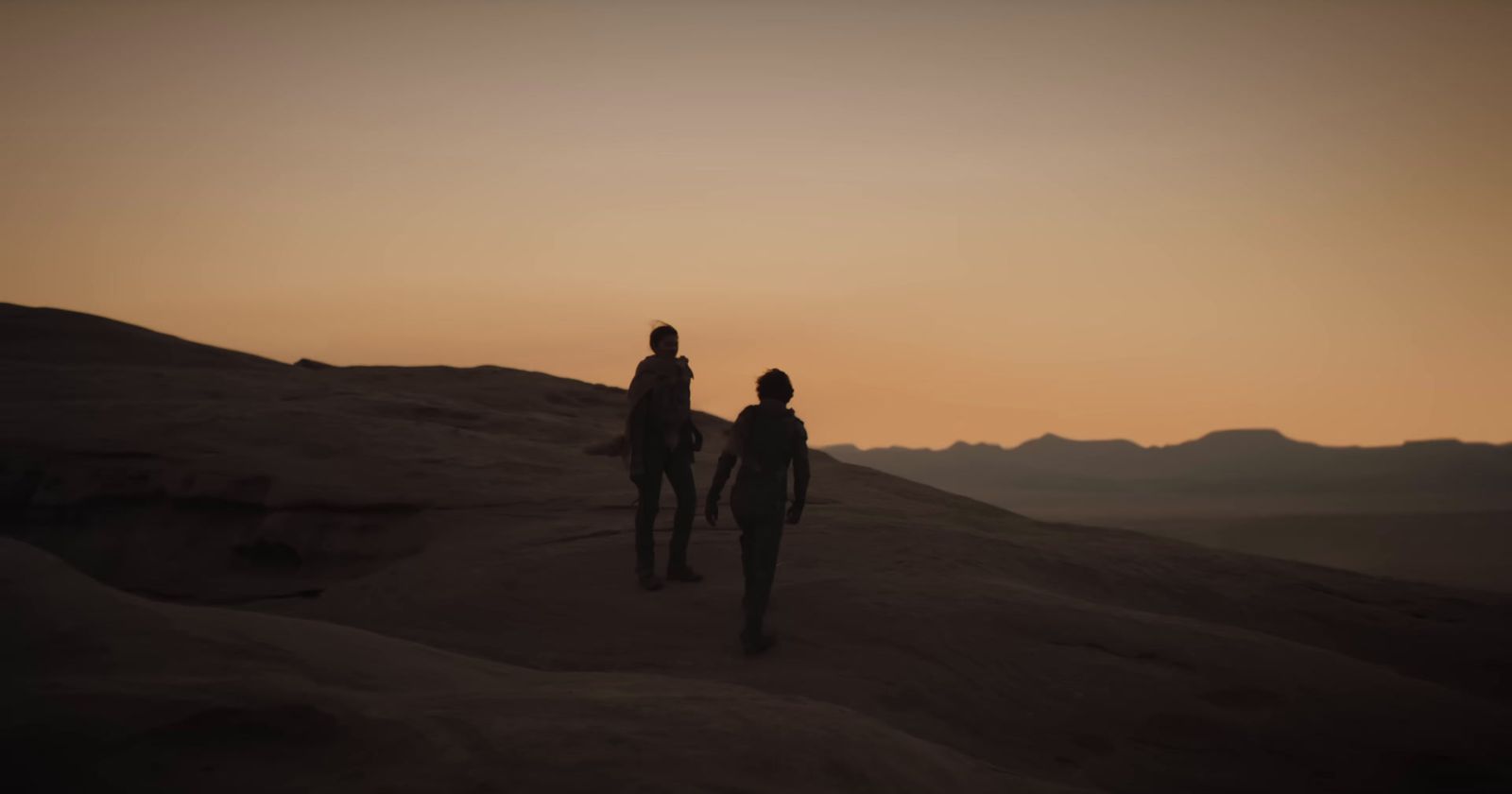 two people walking up a hill at sunset