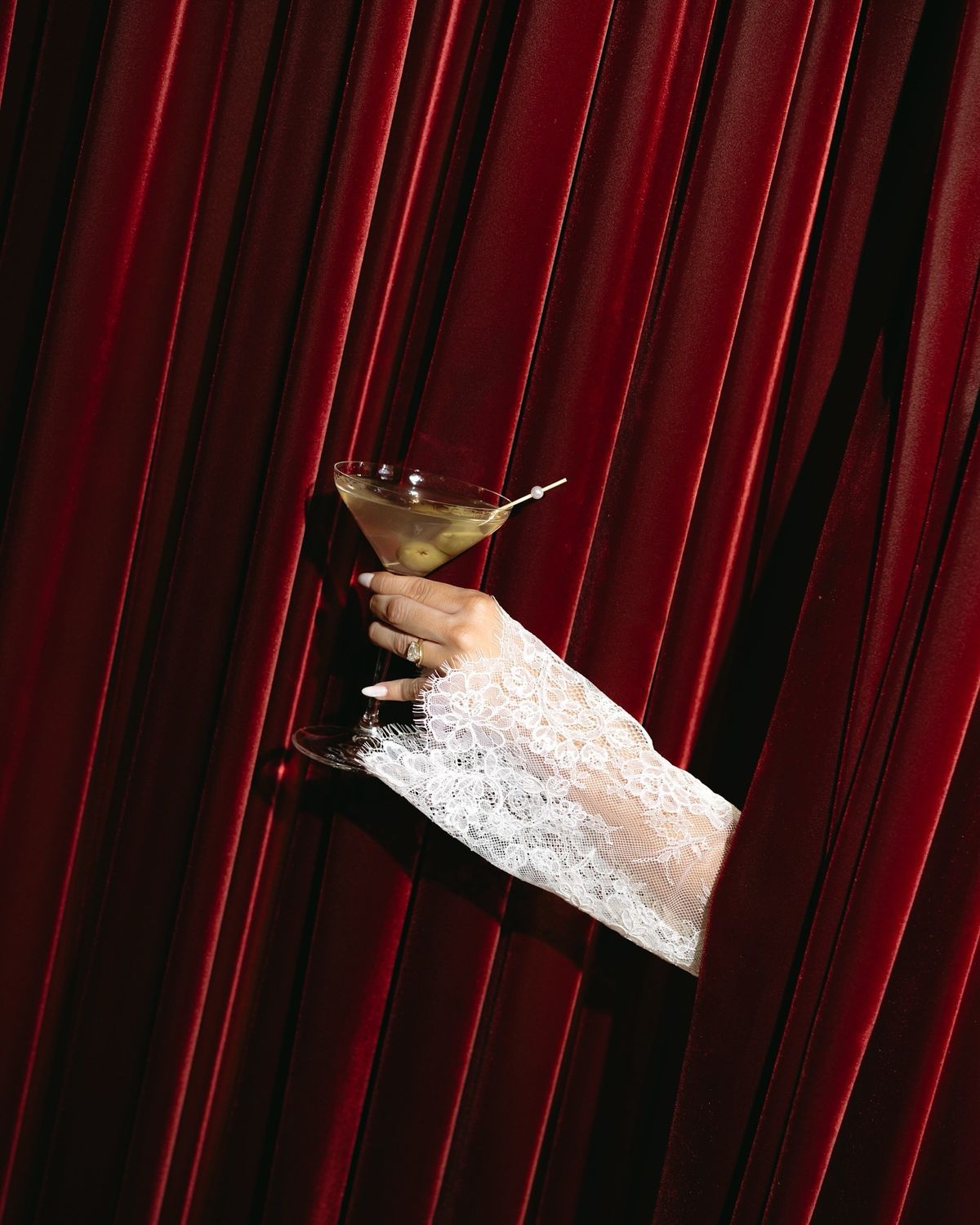a woman's hand holding a martini glass in front of a red curtain